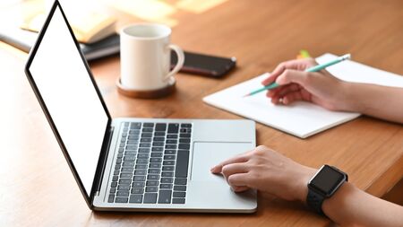 Cropped image of secretary woman's hands while typing on white blank screen computer laptop and...