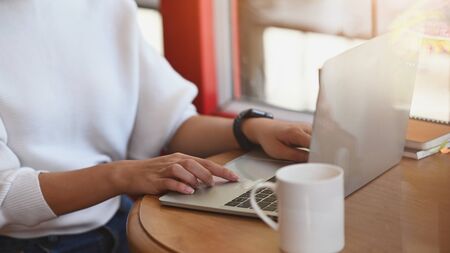 Cropped image of beautiful woman typing on computer laptop while sitting at the orderly wooden table over living room as background.の写真素材