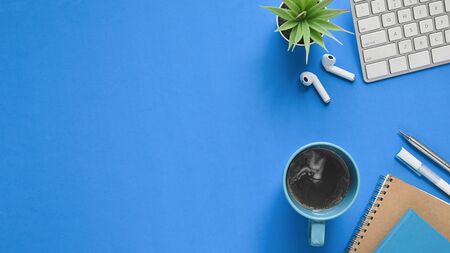 Top view image of workspace. Flat lay coffee cup, pens, pencil, notebook, keyboard, wireless mouse and potted plant on modern blue working table. Orderly workplace concept.の写真素材