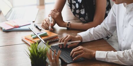 Cropped image of graphic designer team working together by using a computer laptop and tablet with keyboard case at the wooden working desk over orderly living room as background.の写真素材