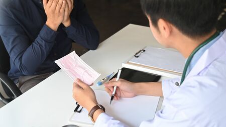 Cropped image of doctor giving a medical mask to his patient while talking/discussing and sitting together at doctor working desk with clipboard and tablet on it.の写真素材