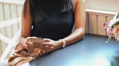 Photo of young brunette woman using a smartphone while sitting at the wooden table in comfortable restaurant. Relaxation woman lifestyle concept.の写真素材