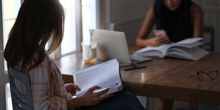 Photo of beautiful women reading a book and relaxing together while sitting at the wooden table over comfortable sitting room as background. Women with relaxing time concept.の写真素材