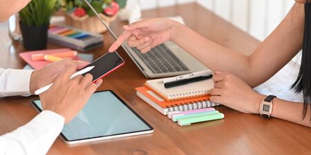 Cropped image of young woman pointing her finger to accountant man's mobile while talking about...