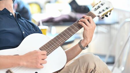Cropped image of smart man relaxing by playing an acoustic guitar while sitting at the modern chair...