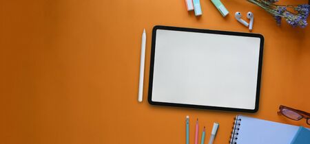 Top view image of white blank screen computer tablet, glasses, marker pens, pencils, notebook and flowers that putting together on colorful working desk. Orderly workspace concept.の写真素材