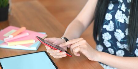 Cropped image of beautiful woman using a smartphone while sitting in front her computer tablet with...
