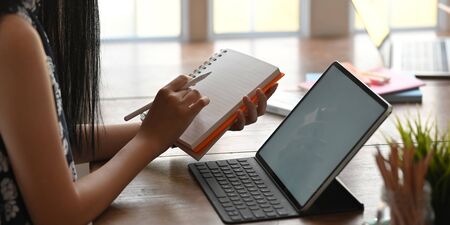 Cropped of beautiful woman writing on notebook that putting on working desk and surrounded by...
