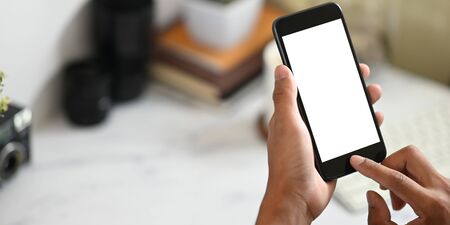 Cropped image of smart man's hands holding a cropped black smartphone with white blank screen over...