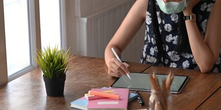 Cropped image of woman with medical mask while drawing/sketching on computer tablet by stylus pen...