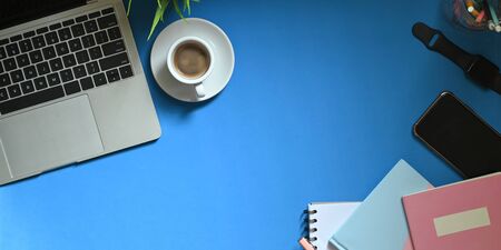 Top view image of computer laptop putting on colorful working desk with coffee cup, potted plant, pencils in glass vase, smartphone, note, smartwatch and notebook. Orderly workspace concept.の写真素材