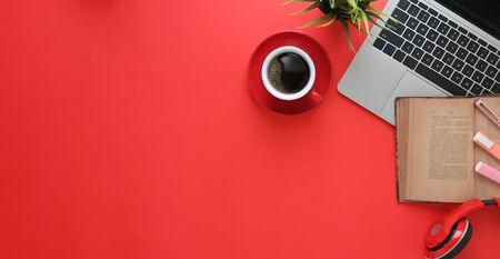 Top view image of computer laptop putting on red working desk with wireless headphone, old book, coffee cup, potted plant. Colorful workspace concept.の写真素材