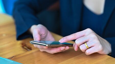Photo of young woman's hands holding and using a smartphone while sitting/relaxing at the wooden...