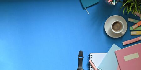 Top view image of white hot coffee cup putting on colorful working desk that surrounded by marker...