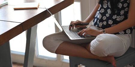 Cropped image of beautiful woman typing on computer laptop that putting on her lap while sitting at...