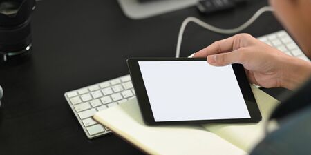 Cropped image of man's hands holding a white blank screen computer tablet and notebook while sitting...