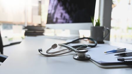 Stethoscope putting on doctor working desk surrounded by clipboard, thermometer, pen, coffee cup,...
