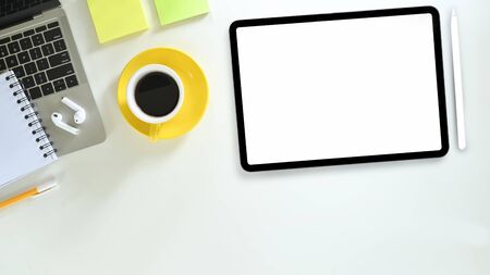 Top view image of computer laptop putting on white working desk that surrounded by note, pen, coffee cup,  white blank screen tablet, stylus pen and wireless earphone. Neat workspace concept.の写真素材