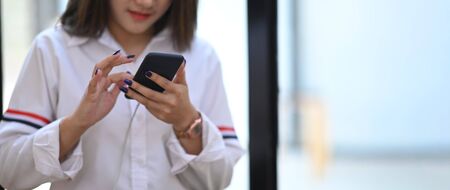 Cropped image of beautiful woman holding a smartphone in her hands while standing/relaxing over...