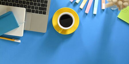 Top view image of hot coffee cup putting on colorful working desk and surrounded by computer laptop,...