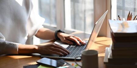 Cropped image of stylish woman typing on computer laptop while sitting at the wooden working desk...