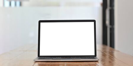 White blank screen computer laptop putting on wooden working desk over comfortable office glass wall...