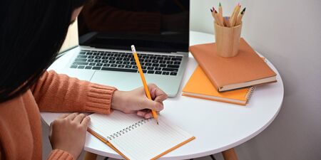 Cropped image of attractive woman taking notes while sitting at the white working desk over...