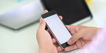 Cropped image of smart man's hands holding a white blank screen smartphone while sitting in front of...