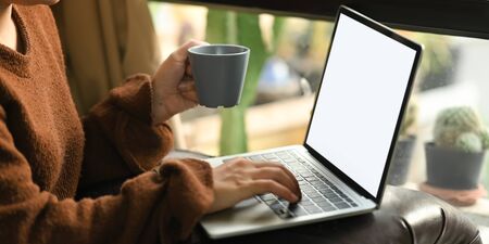 Cropped image of beautiful asian woman holding a coffee cup in hand while sitting in front her...