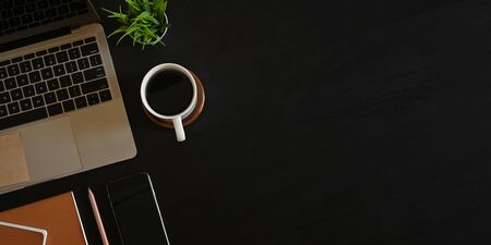Photo of Computer laptop with black empty screen putting on black working desk that surrounded by coffee cup, potted plant, notebook, pencil and black empty screen smartphone.の写真素材