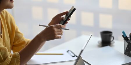Photo of stylish woman holding a smartphone and stylus pen in hands while sitting in front her...