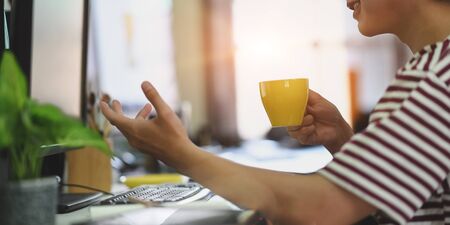 Cropped image of smart man in striped t-shirt drinking a hot coffee while sitting and working with...