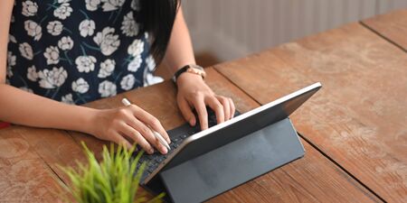 Cropped image of stylish woman holding a stylus pen and typing on computer tablet keyboard case...