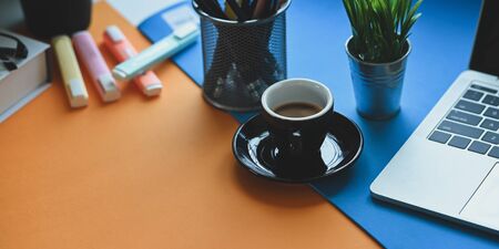 Coffee cup putting on two tone working desk that surrounded by computer laptop, potted plant, pencil...