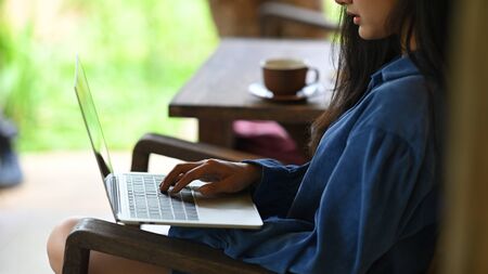 Close-up woman is using a computer laptop while sitting at the wooden chair.