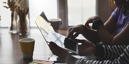 A young couple is working together with a computer laptop and tablet at the wooden working desk.の写真素材