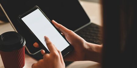Cropped image of woman holding a white empty screen smartphone in her hands. Woman using mobile with...