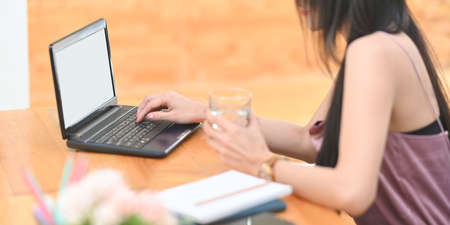 A woman is typing on a white blank screen computer laptop at the wooden working desk.の写真素材
