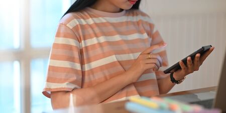 Cropped image of university student holding a smartphone in her hands. Woman relaxing with mobile phone at home concept.の写真素材