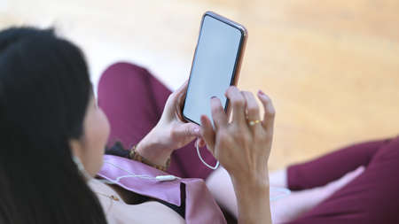 The top view image of a woman is relaxing with a white blank screen smartphone in the living room.の写真素材