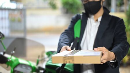 A delivery man is giving a parcel to a customer while standing next to his motorcycle.の写真素材