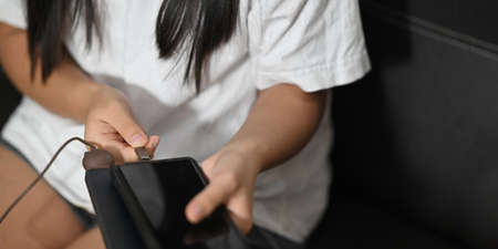 A woman's hands are charging a smartphone while sitting at the black leather sofa.