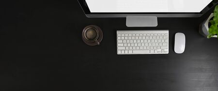 Top view image of white blank screen computer monitor and office equipment are putting on the black table.の写真素材