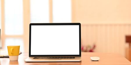 Blank screen computer laptop is putting on a wooden working desk surrounded by a coffee cup,...