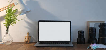 A white screen computer laptop is putting on a wooden working table surrounded by various equipment.の写真素材
