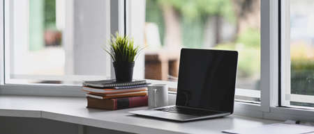 Laptop with a black screen is putting on a windowsill surrounded by various equipment.