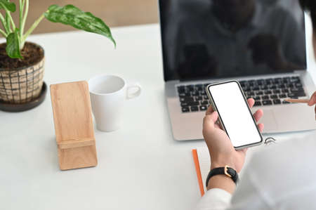 Cropped shot man holding and using mockup mobile phone with blank white screen in office.
