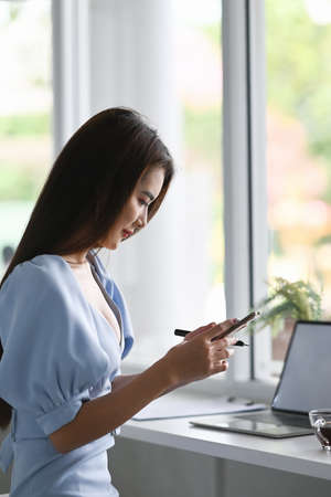 Side view of young female freelancer using smartphone while sitting in modern working space.