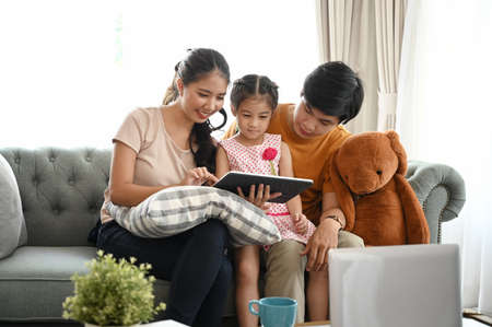 Family using digital tablet. Parents showing digital tablet to their daughter on couch at home.の写真素材