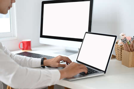 Cropped shot of hands typing on laptop with blank screen on work space.